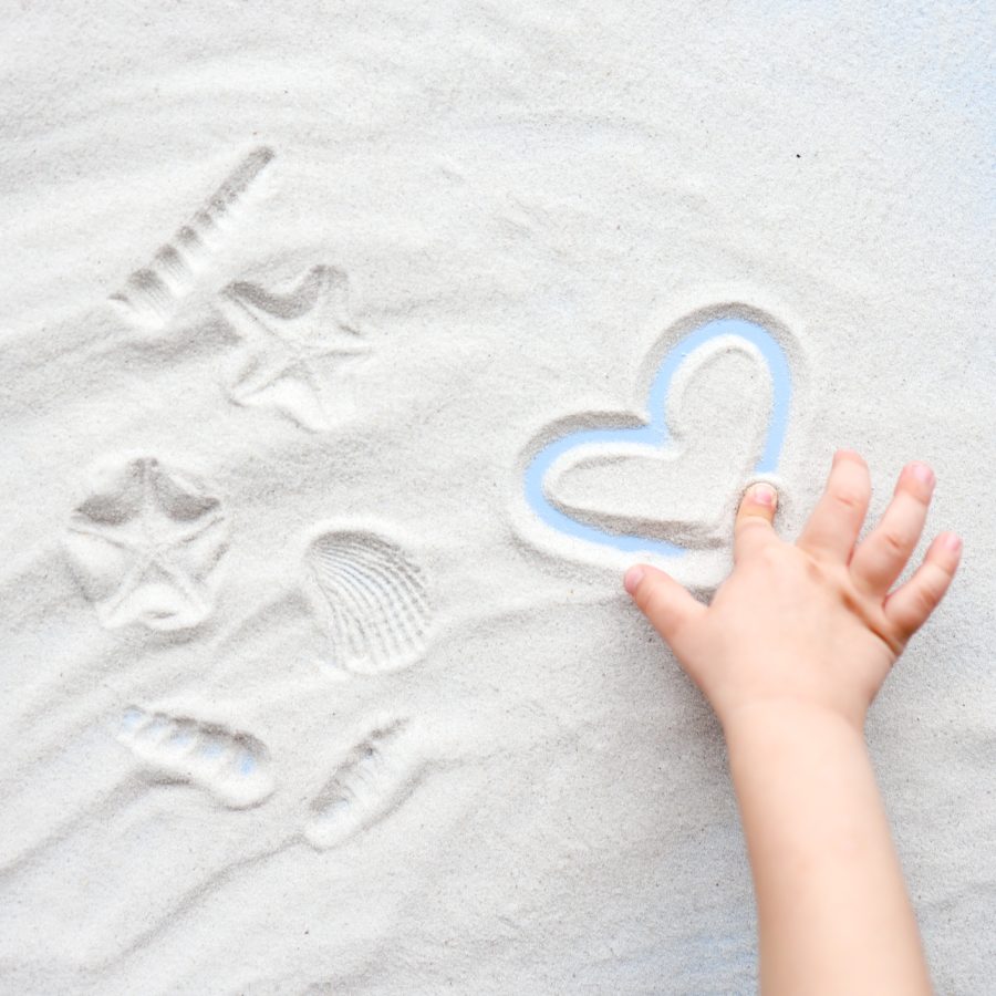 Child plays with sand, draws a heart.